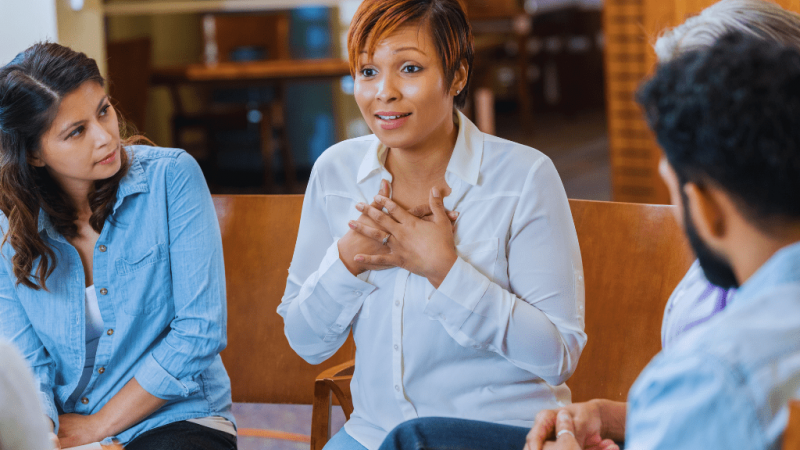 A woman sharing her personal experience during a group rehab session, supported by attentive listeners. This reflects the compassionate environment fostered by Berea Kentucky Drug and Alcohol Rehab Resources.