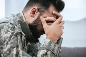 veteran wearing military clothing with head in his hands experiences symptoms of PTSD