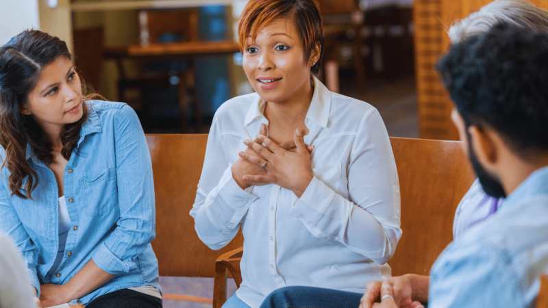 A woman sharing her personal experience during a group rehab session, supported by attentive listeners. This reflects the compassionate environment fostered by Berea Kentucky Drug and Alcohol Rehab Resources.